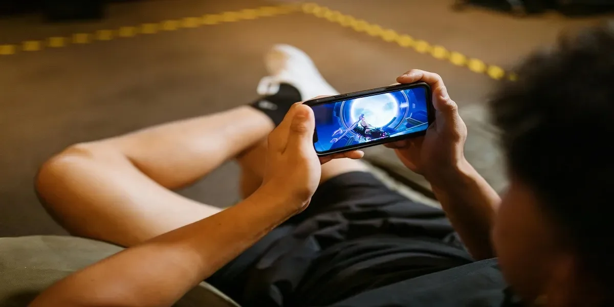 A person reclined on a couch, holding a smartphone horizontally to play a video game